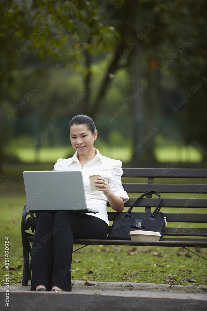 Mid adult businesswoman working in the park during coffee break Mid adult businesswoman working in the park during coffee break