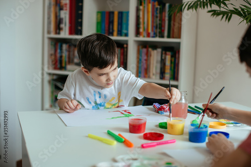 Left handed little boy reaching for yellow paint with paintbrush in his hand.