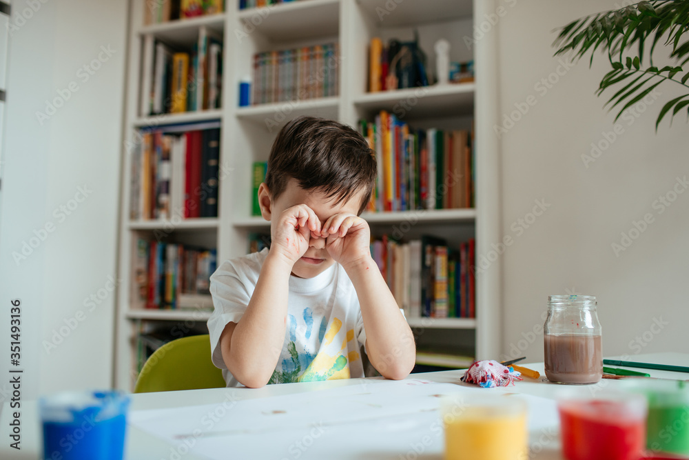 Little boy rubs his eyes while losing concentration after doing school painting assignments. Little boy rubs his eyes while losing concentration after doing school painting assignments.