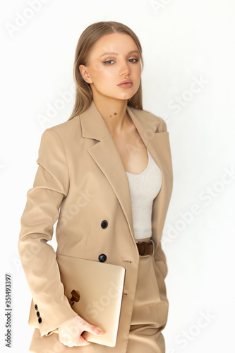 Beautiful woman businesswoman in a beige suit holds a laptop in her hand and looks at the camera. Isolated on a white background. A great example of office wear.