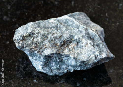 closeup of sample of natural mineral from geological collection - unpolished gray Basalt rock on black granite background