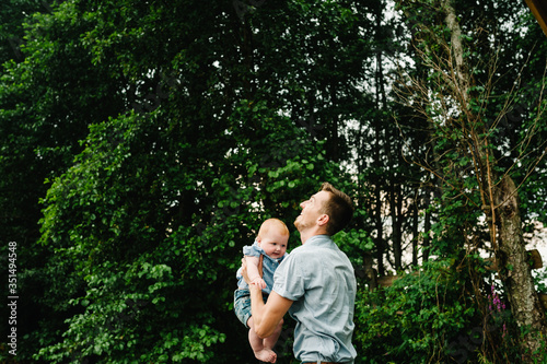 Father throws baby in nature, girl flies in the sky. Portrait dad with child together. Daddy, little daughter outdoors. Young father with baby girl walk in park. Family holiday in garden or forest. © Serhii
