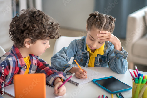 Boy and girl sitting at round table with tablets, preparing their assignments