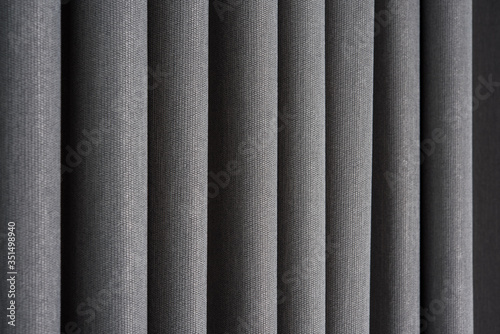 Closeup view of curtain in thin and thick vertical folds made of dense fabric.Textured materials and textiles abstract backgrounds.