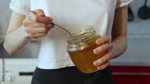 woman takes honey with a spoon from a jar and adds it to the dish