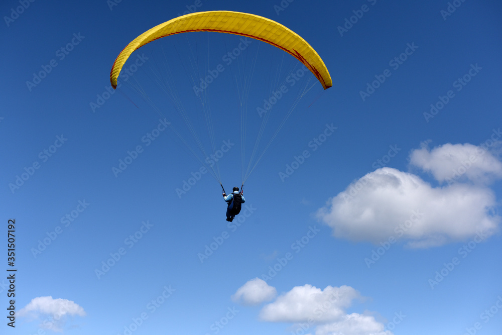 Paraglider flying over fields in sunny day. Paraglider in the blue sky. Paraglider flying over fields in sunny day. Paraglider in the blue sky.