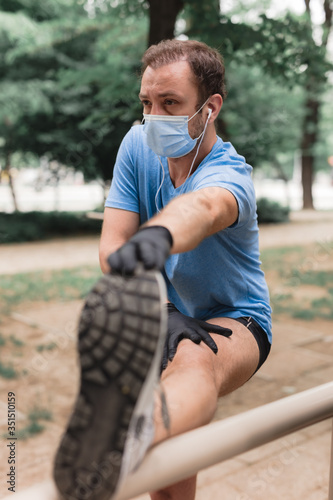 Sportsman with medical mask and gloves, smartphone and earbuds working out, jogging in urban surroundings.