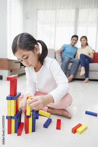 Girl playing with building blocks while parents look on