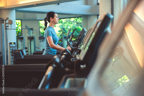 Attractive young sports woman is working out in gym doing cardio training running on treadmill in sport club