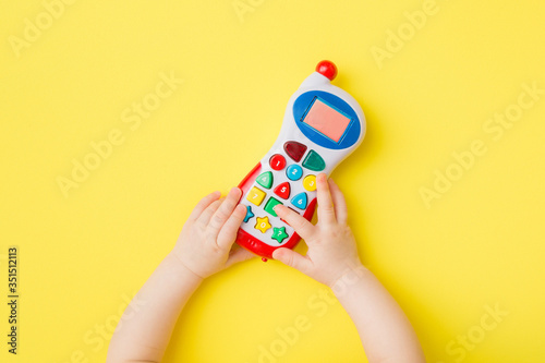 Baby hands playing with colorful toy of mobile phone on bright yellow table background. Closeup. Point of view shot. Top down view. photo