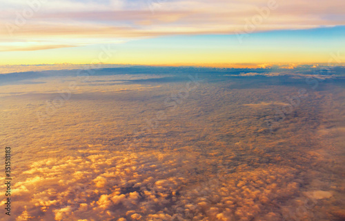 Top view of fluffy clouds on sunset sky view from flying airplane window