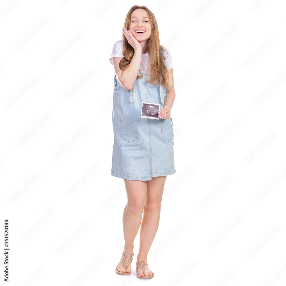 Fototapeta premium Pregnant woman in denim sundress standing looking smiling, holding ultrasound picture on white background isolation