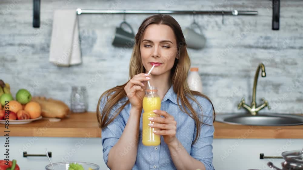 Portrait of smiling young blonde woman drinking fresh orange juice. Medium shot on RED camera Portrait of smiling young blonde woman drinking fresh orange juice. Medium shot on RED camera