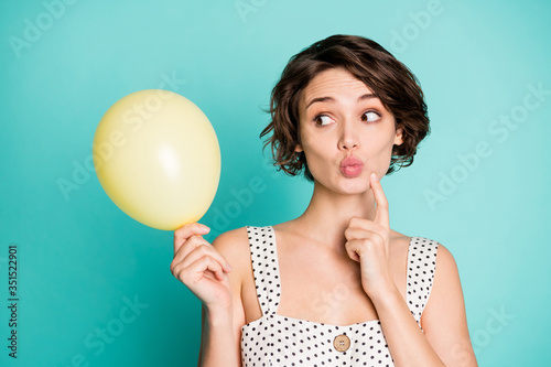 Closeup photo of pretty lady holding big yellow balloon bubble look side finger on chin tricky person wear casual white dotted singlet isolated pastel teal color background © deagreez