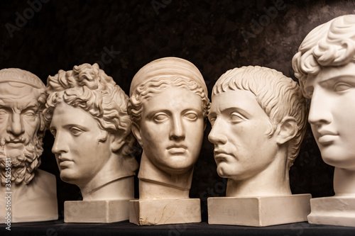 Group gypsum busts of ancient statues human heads for artists on a dark background. Plaster sculptures of antique people faces. Renaissance epoch style. Academic subject. Blank for creativity.