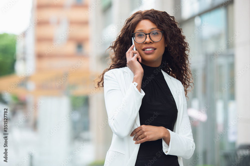 Fototapeta premium Talking phone. African-american businesswoman in office attire smiling, looks confident and serious, busy. Finance, business, equality and human rights concept. Beautiful young model, successful.