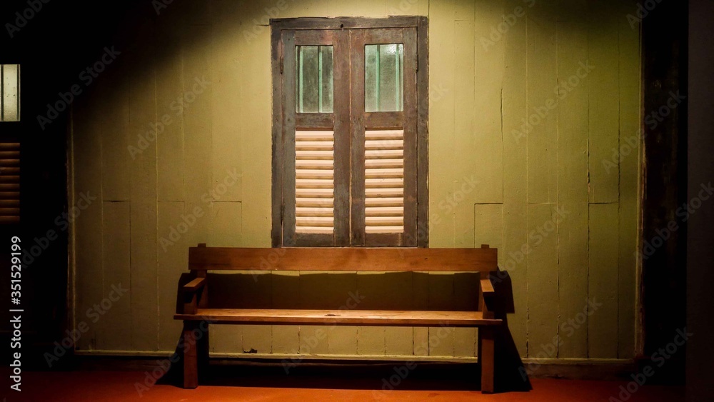 A wooden bench under a light and window
