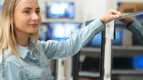 Smart modern female customer choosing large TV-sets at electronics store