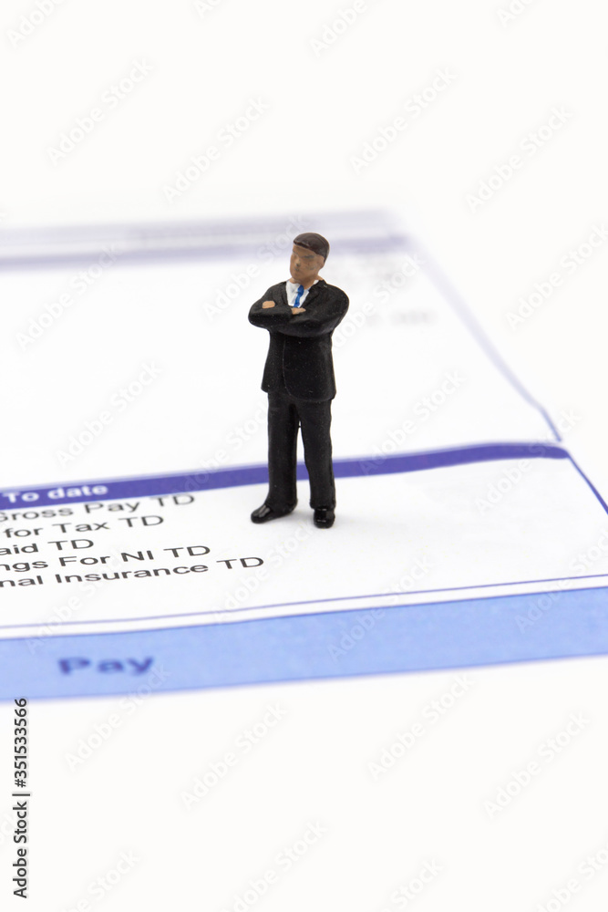 Miniature scale model businessman standing on a wage pay slip showing earnings deductions. Isolated on a white background Miniature scale model businessman standing on a wage pay slip showing earnings deductions. Isolated on a white background