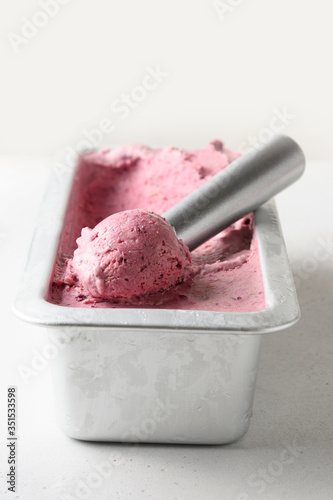 Homemade berry ice cream in metallic tub with scoop. Close up. Vertical.