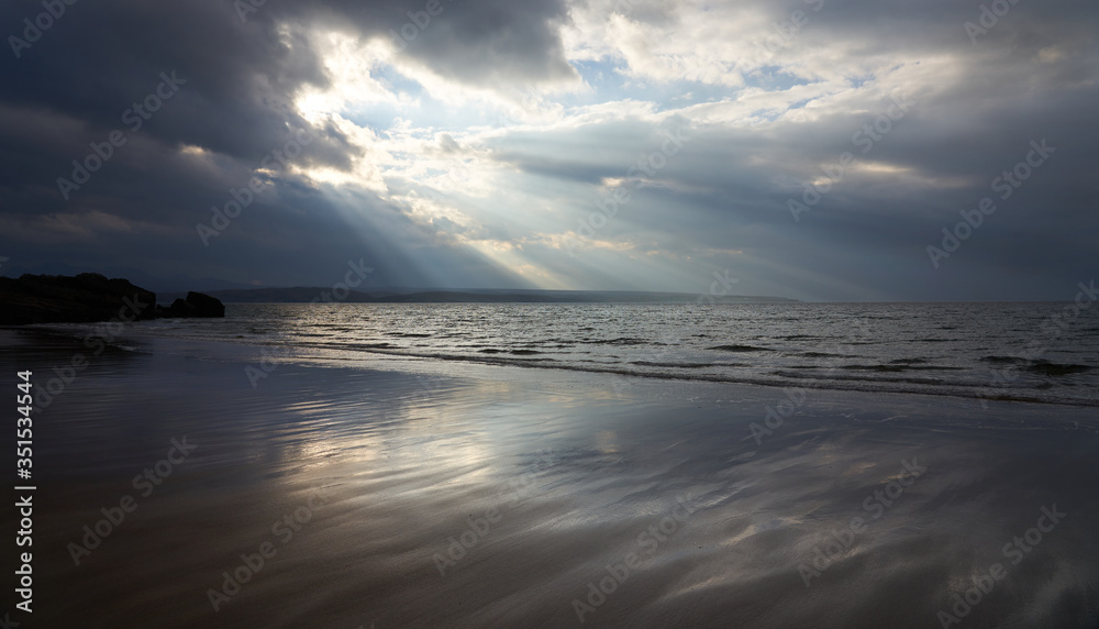 Rays of autumn sunlight breaking through the cloud aover the wet beach of Big Sand near Gairloch in the Scottish Highlands, Scotland, UK.