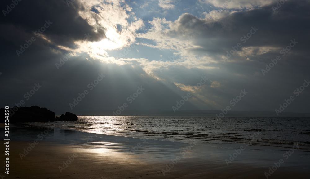Obraz premium Promienie jesiennego światła słonecznego przebijające się przez chmurę na mokrej i kamienistej plaży Big Sand w pobliżu Gairloch w Scottish Highlands, Szkocja, Wielka Brytania.