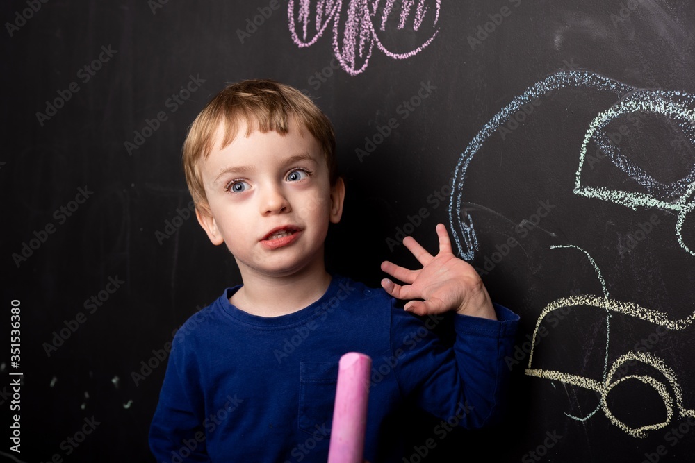 Little boy learns to draw with chalk on a black slate wall. Children's colorful drawings. drawing lessons. the child shows his drawing on the wall. European appearance. close-up.