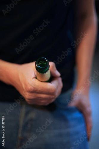 Close up of male hand holding a full green glass beer bottle. 