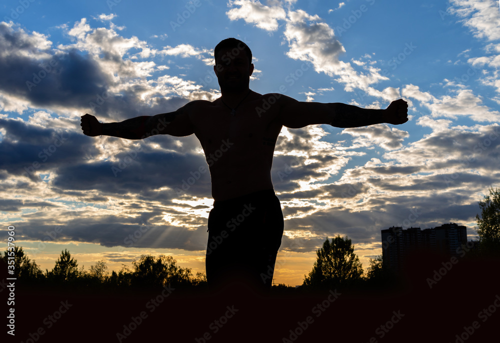 Silhouette of a strong muscular man on a background of sunset sky. Fitness in the evening on the street. Silhouette of a strong muscular man on a background of sunset sky. Fitness in the evening on the street.