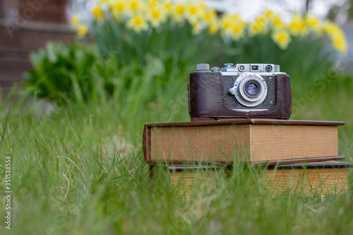 Old-fashioned camera and the old books in the grass.Sunny spring time day. Vertical.