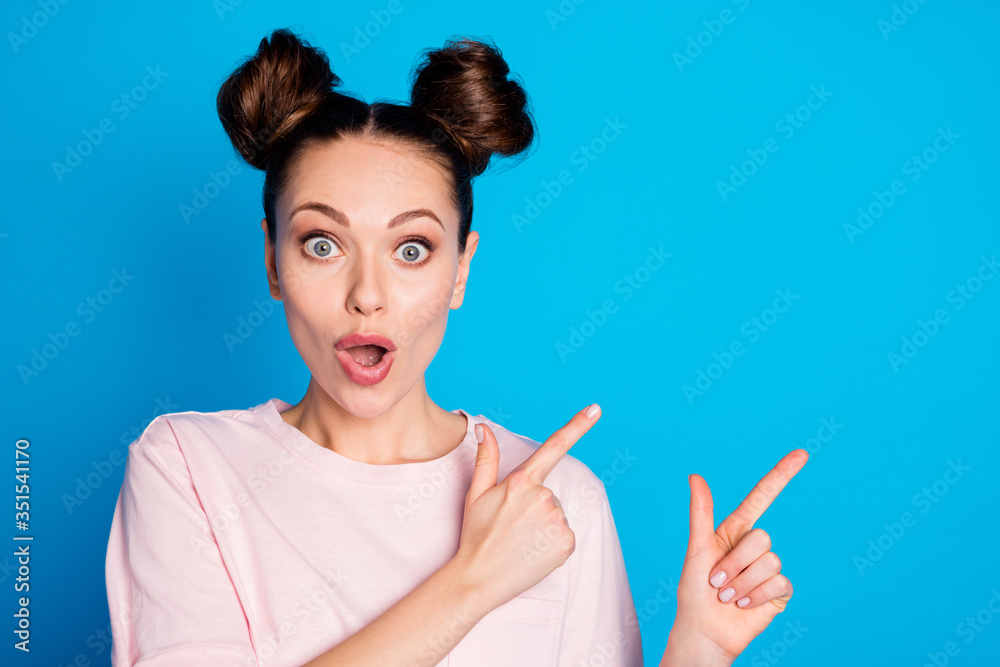Closeup photo of attractive pretty shocked lady two funny buns direct finger side empty space showing novelty sale product wear casual white pink t-shirt isolated blue color background Closeup photo of attractive pretty shocked lady two funny buns direct finger side empty space showing novelty sale product wear casual white pink t-shirt isolated blue color background