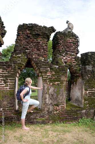 A blonde traveler without shoes looks at a wild monkey among the ancient ruins.