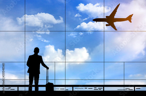 Silhouette of businessman standing at the terminal airport with airplane background, hand holding the luggage during waiting for flight boarding time, business and travelling concept.