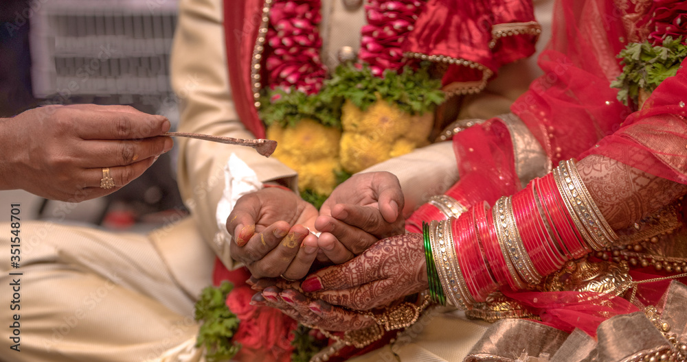 Traditional Indian wedding scene where a beautiful couple is taking part in Hindu rituals of their marriage ceremony. Bride has wore colorful nuptial bangles, while the couple is receiving holy water