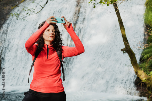 Woman taking photo with mobile phone in front of a waterfall