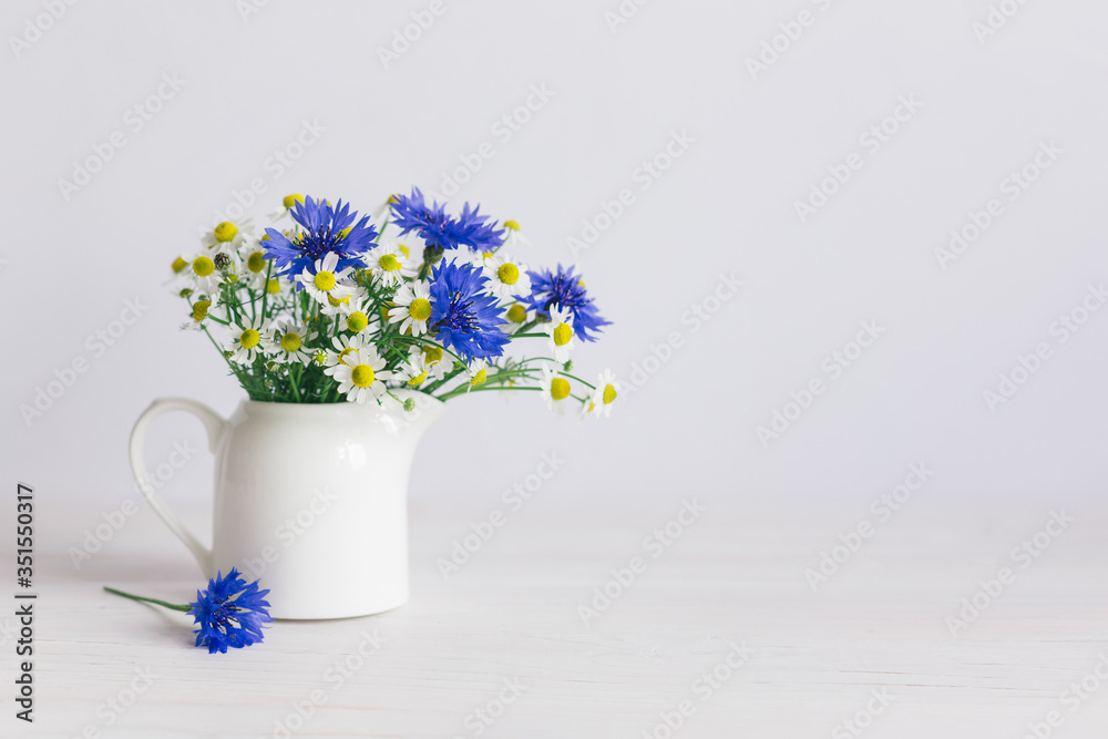 Romantic bouquet of the meadow flowers in a jar on a white background. Chamomiles and Cornflower in a jar. Romantic bouquet of the meadow flowers in a jar on a white background. Chamomiles and Cornflower in a jar.