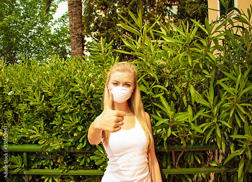 Young woman in protective mask making like symbol. Nature green background. Coronavirus concept.
