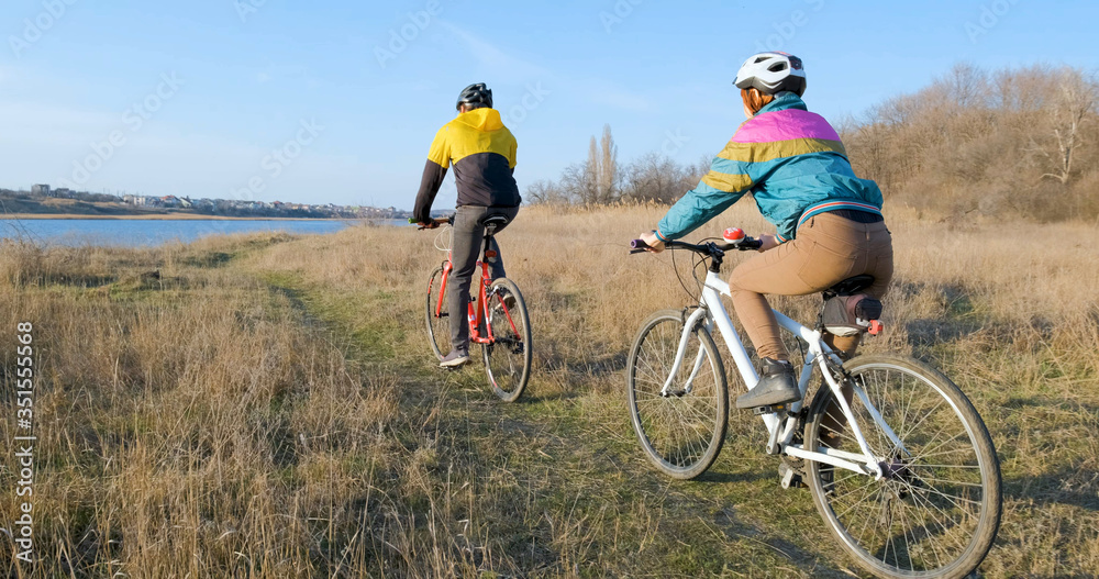 Couple of male and female ride on bicycles near river during sunset Couple of male and female ride on bicycles near river during sunset