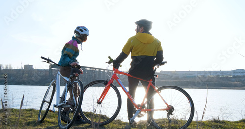 Couple of male and female ride on bicycles near river during sunset 