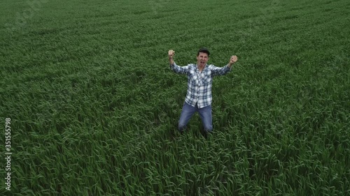A man farmer on a green wheat field rejoices in the emergence of grain crops, jumps up. Happy agronomist on farmland, top view. The concept of agribusiness.