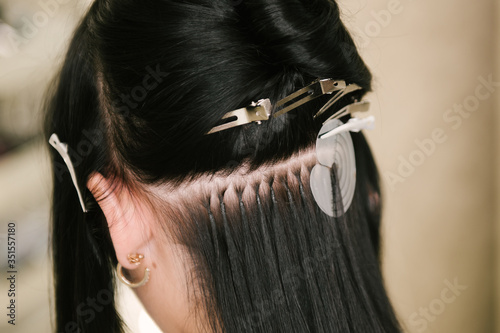 The hairdresser does hair extensions to a young girl in a beauty salon. Professional hair care. Close up of capsules and strands of grown hair