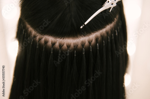 The hairdresser does hair extensions to a young girl in a beauty salon. Professional hair care. Close up of capsules and strands of grown hair photo