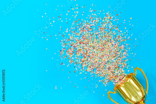 image of little gold cup , concept for winning or success. Golden trophy cup and streamers on blue background, top view with space for text photo