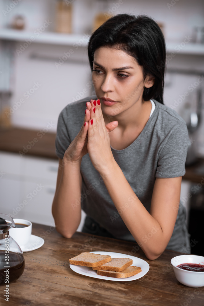 selective focus of pensive woman with bruise on face near breakfast on table, domestic violence concept