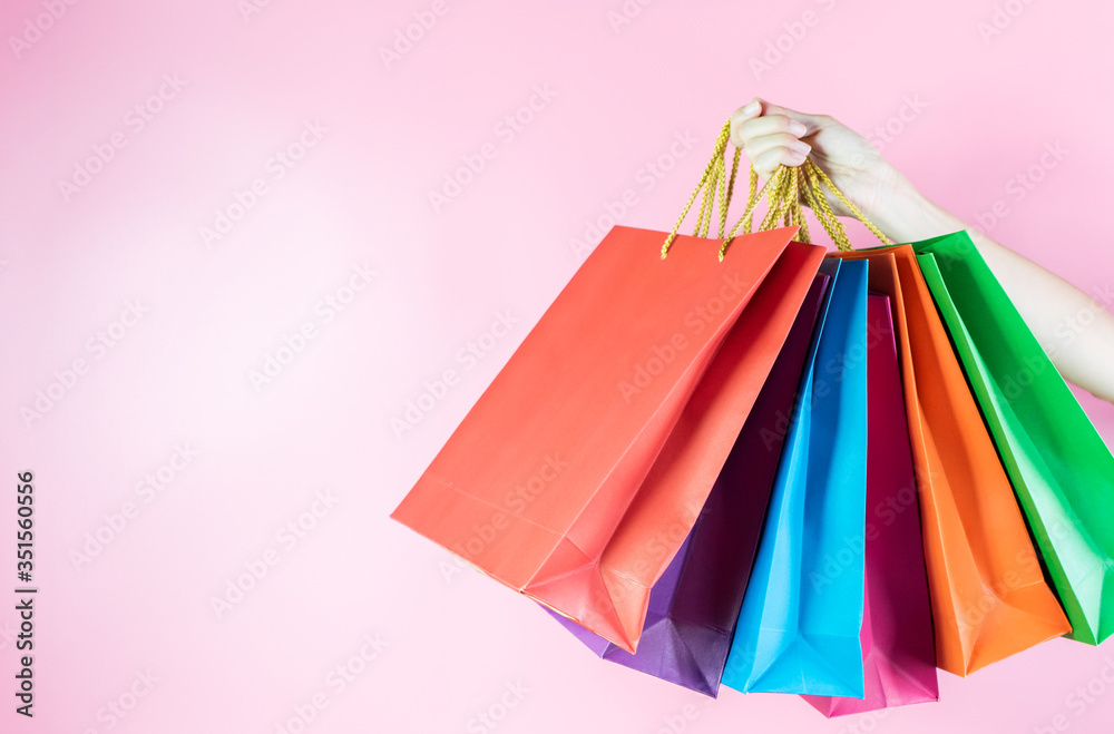 Close up hand holding colorful shopping bags on pink background with copy space.