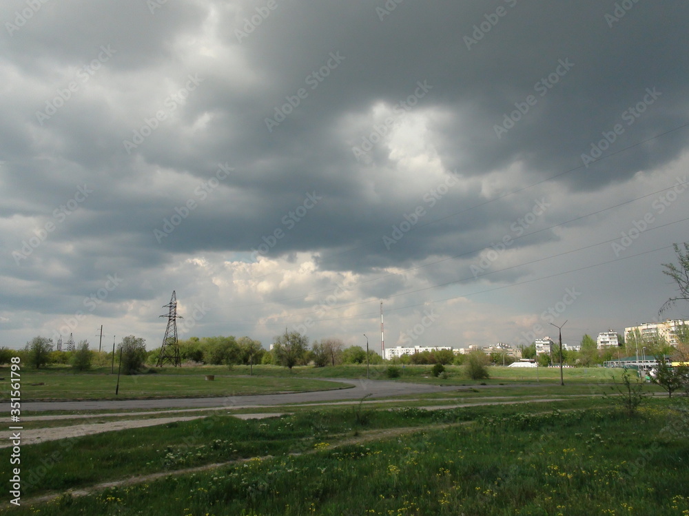 Landscape of the outskirts of the city illuminated by the sun against a cloudy storm sky.
