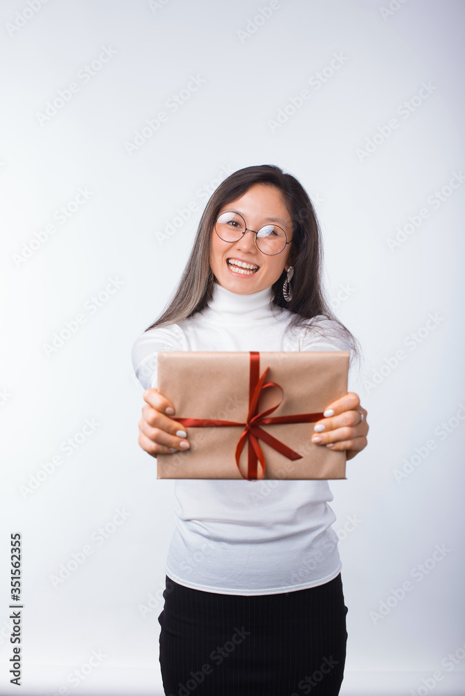Fototapeta premium Excited girl wearing round glasses is holding a wrapped gift over white.