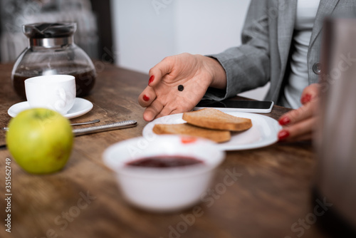 selective focus of woman with black dot on palm touching plate with toast bread near apple, jam and coffee pot, domestic violence concept