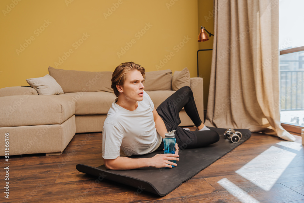 Φωτογραφία young man lying on fitness mat and holding sports bottle with water, end of quar