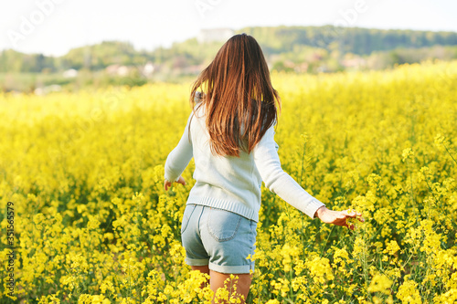 Spring portrait of happy young woman posing in colza field, back view © annanahabed